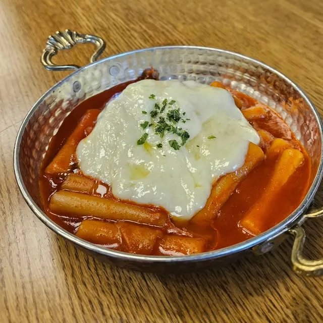 Tteokbokki in scharfer roter Sauce mit geschmolzenem Käse in einer Kupferpfanne